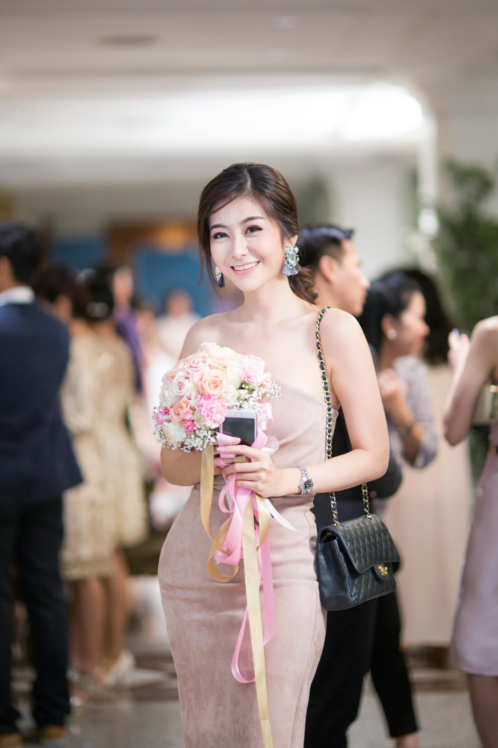 An elegant woman in a stylish dress at a social event, holding a bouquet.