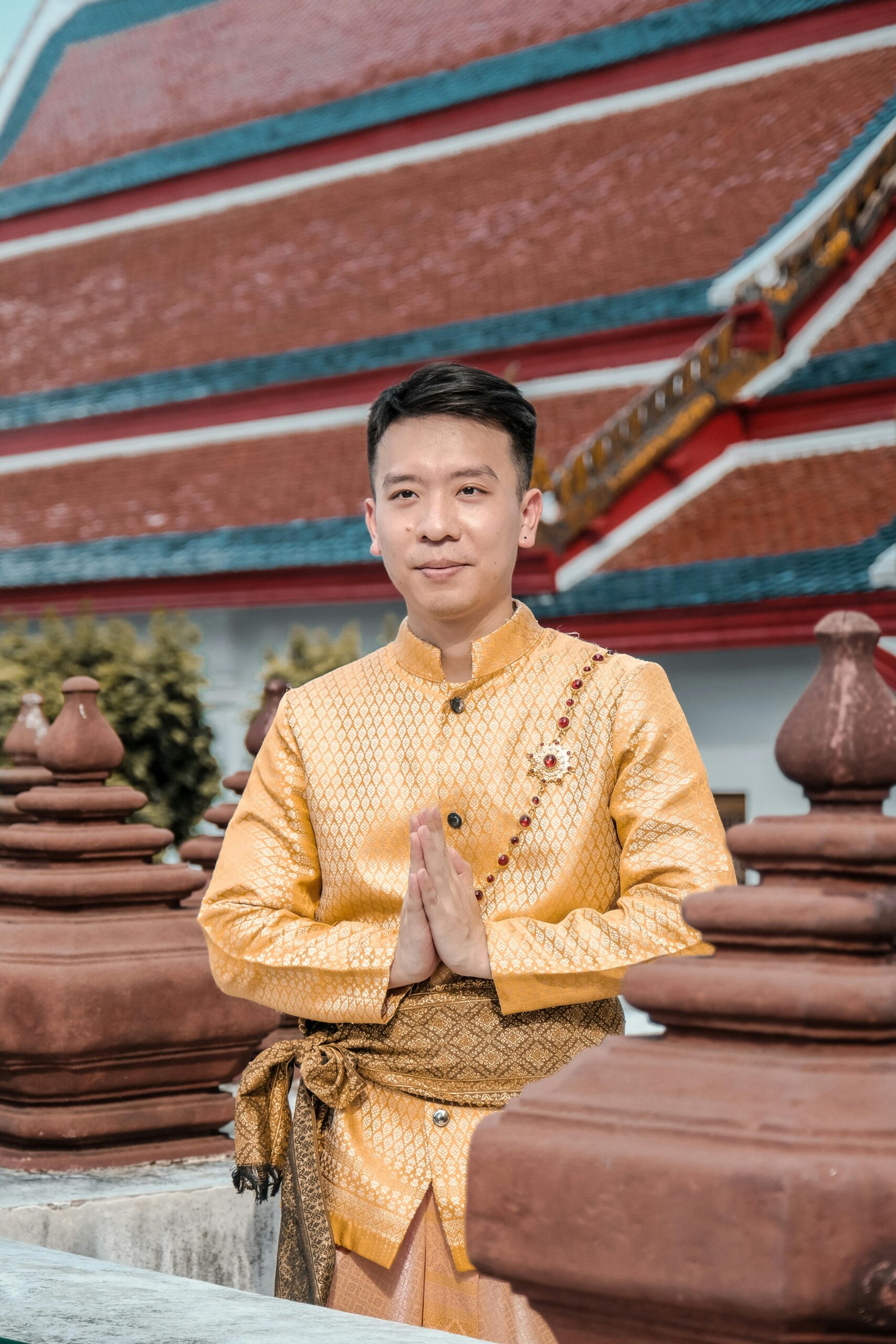 Man in traditional Thai clothing posing with a temple backdrop.